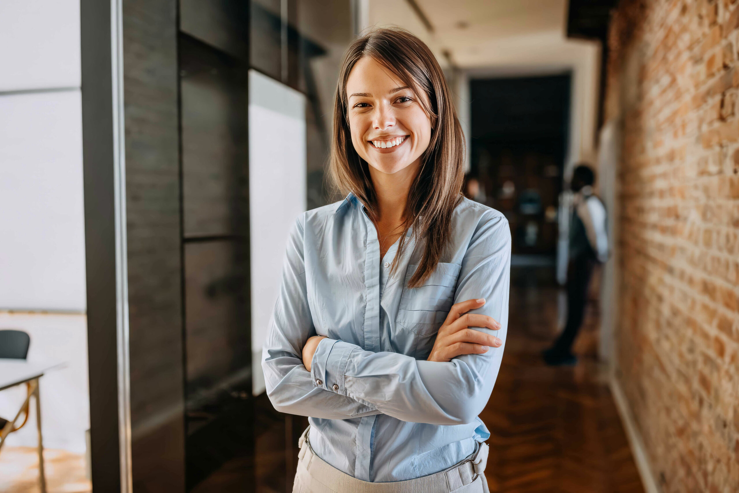 Femme souriante bras croisés dans un couloir de bureaux, photographie d’ambiance pour Consultimo